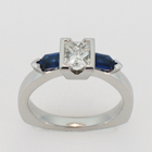 Platinum diamond ring with step-cut tapered bullet-shaped blue sapphire sides.
