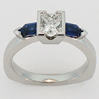 Platinum diamond ring with step-cut tapered bullet-shaped blue sapphire sides.