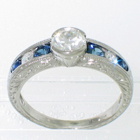 Platinum diamond ring with 0.62 carat round brilliant diamond in bezel setting on hand-engraved tapered-channel shank with 0.30 carat total weight of round blue sapphire melee and 0.20 carat total weight of round diamond melee