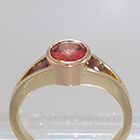 14 Karat 2-tone Yellow and Rose Gold 3-stone ring with round Padparadscha Sapphire in full bezel setting and orange diamonds channel-set into split-shank
