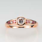 14 karat rose gold ring with a bezel-set round diamond and a tapered channel of alternating pink and colorless diamonds.