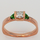14 karat rose gold knife-edge saddle ring with a princess-cut diamond and two natural green colored diamond trilliants.
