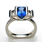Platinum ring with emerald-cut blue sapphire and trapedoid-shaped side diamonds in w-shaped saddle setting.
